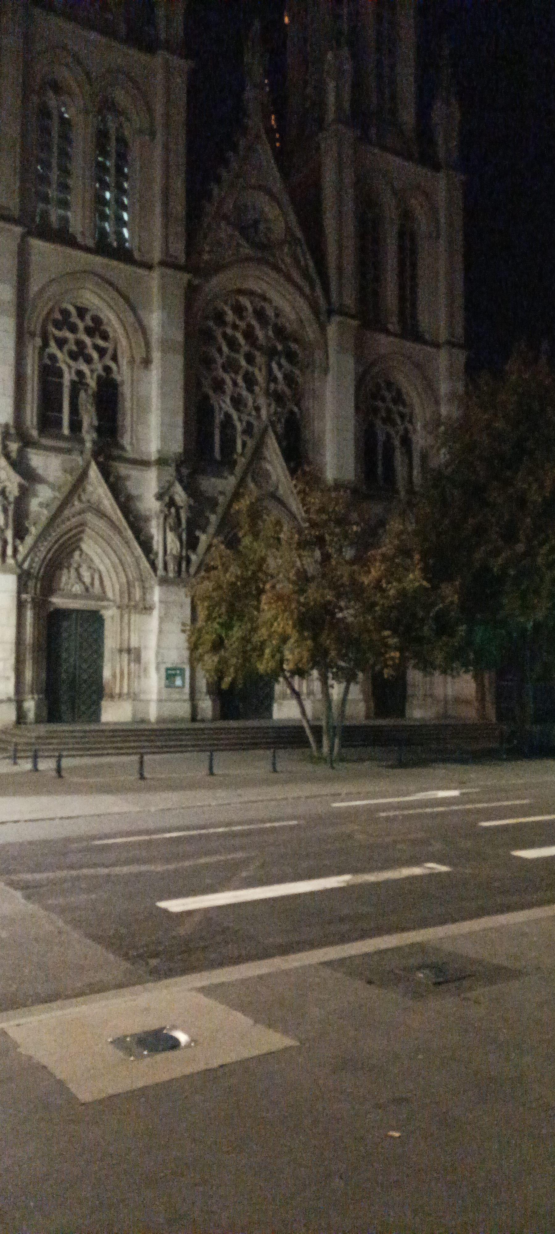 Photo d'église néo-gothique prise de nuit depuis l'autre côté de la rue. Au premier plan les zébras d'un arrêt d'autocar.